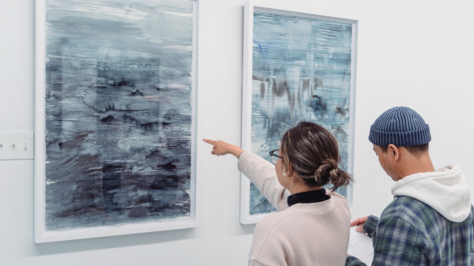 A woman in a gallery intently observes abstract paintings, highlighting her engagement with modern art